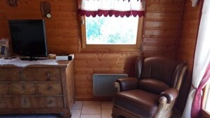 Una habitación de cabaña de madera con una butaca de cuero, un aparador de madera y un televisor sobre un mueble bajo.