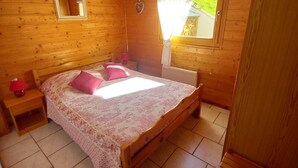 Un dormitorio de cabaña de madera con cama, mesita de noche, espejo y ventana con cortinas.