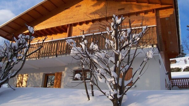 Una cabaña de madera con balcón, rodeada de árboles cubiertos de nieve.