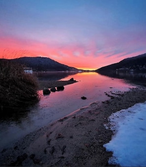 Ein Fluss bei Sonnenuntergang, ruhiges Wasser und ein verschneiter Uferbereich.