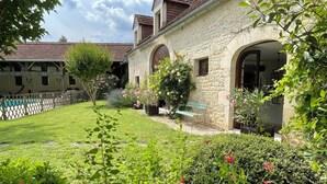 Un edificio de piedra con arcos, una valla de madera y un césped con plantas florecientes.