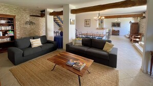 Un amplio salón con dos sofás, una mesita de centro y una estantería. Una escalera conduce a un nivel superior.