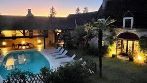 Un área de piscina con sillones de descanso, un comedor y un edificio con chimenea.