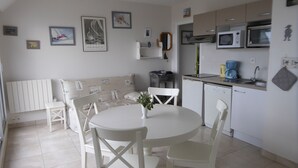A compact kitchen with white appliances, a dining area with a round table and chairs, and nautical-themed wall art.