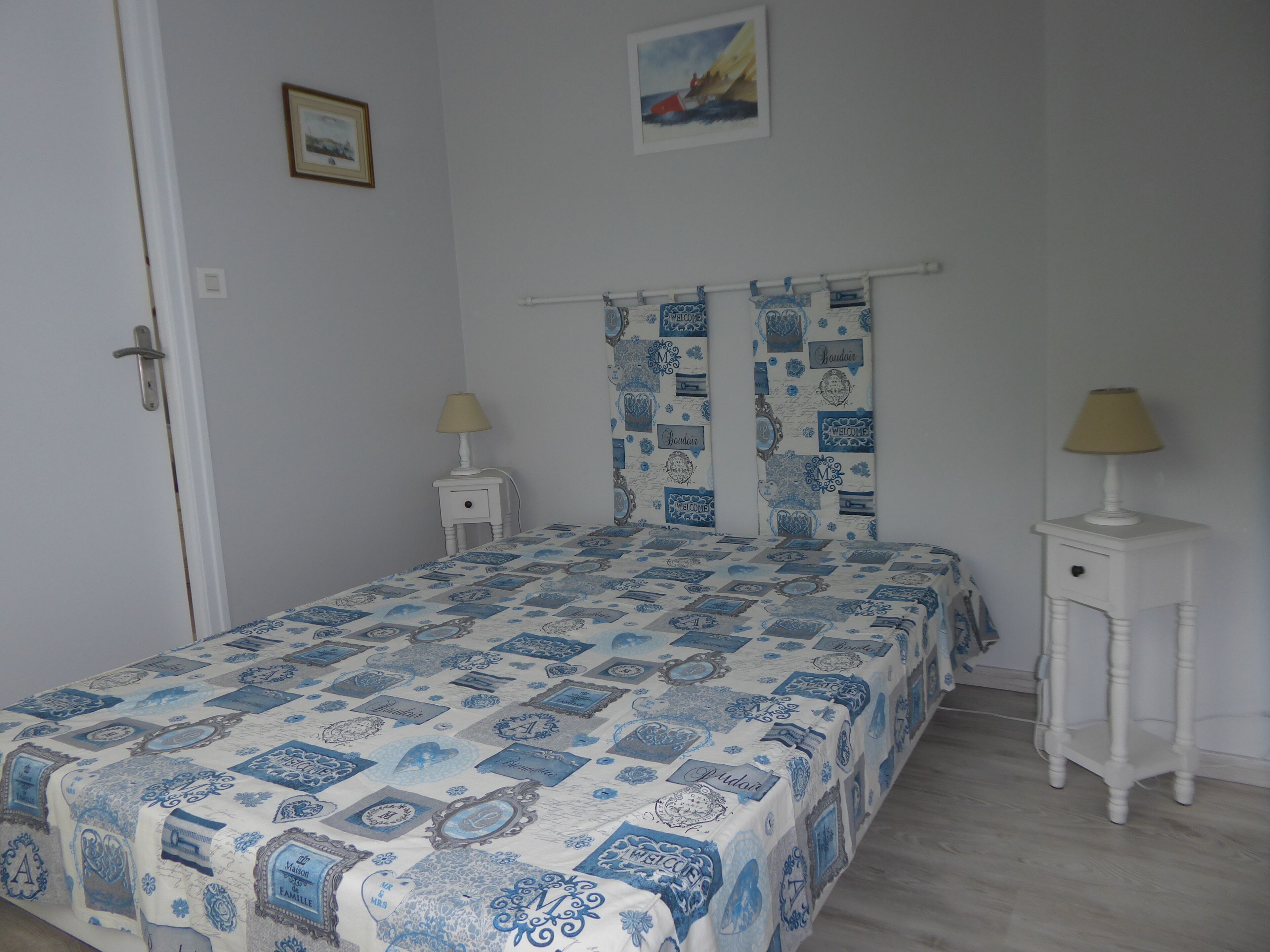 A bedroom with a bed, two bedside tables, a door, and a wall with a framed picture.