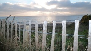 A wooden fence with barbed wire, overlooking a beach with the ocean and a cloudy sky.