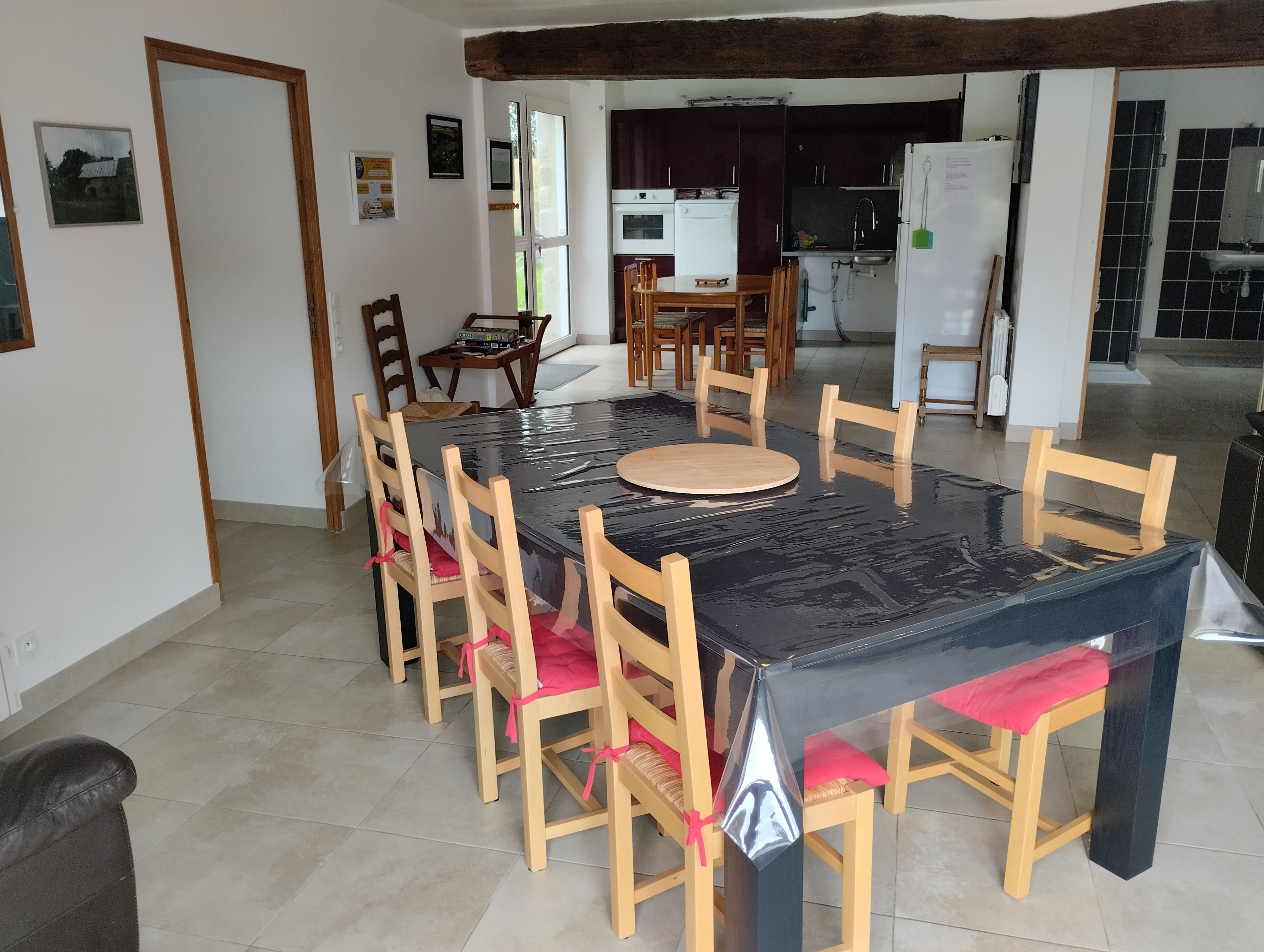 Un coin repas avec une table noire et des chaises en bois, une cuisine en arrière-plan et une porte donnant sur l’extérieur.