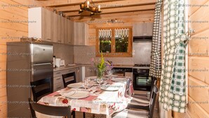 Interior de madeira com uma mesa de jantar posta para quatro, geladeira, fogão e janela com cortinas de renda.