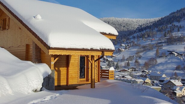 A wooden cabin with a snow-covered roof, surrounded by a snowy landscape and a clear blue sky. - La Bresse Spacious And Comfortable Chalet (La Bresse)