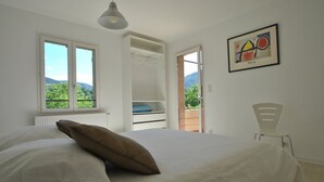 Ein Schlafzimmer mit einem Bett, einem Fenster, einer Tür, die auf einen Balkon führt, und einem gerahmten Kunstwerk an der Wand.