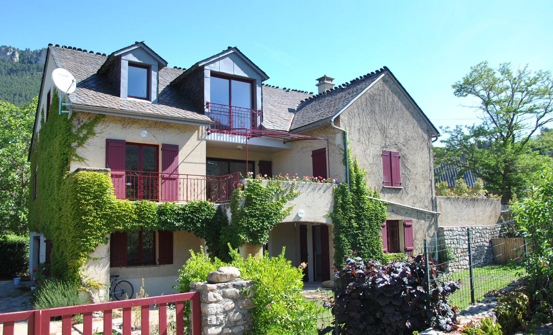 A two-story house with a balcony, stone walls, and a red gate.