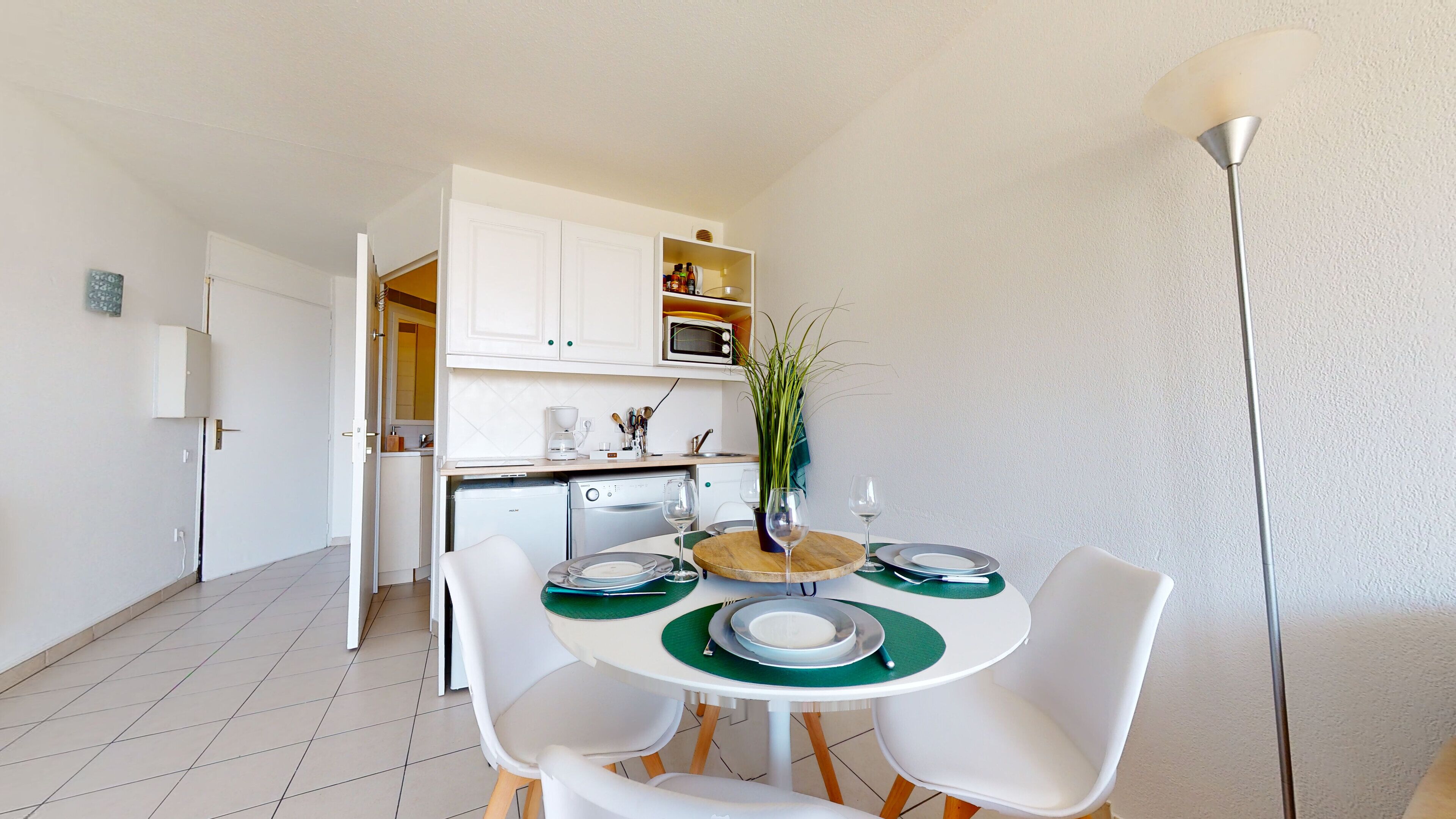 A compact kitchen with white cabinets, a microwave, and a coffee maker. There is a dining table with four chairs and a vase with a plant.
