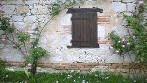 A rustic stone wall with a wooden window and pink flowers growing around it. - Comfortable space and well decorated (Castelsagrat)