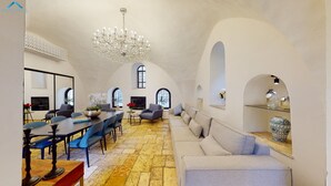A spacious living area with a high ceiling, a chandelier, a dining table with chairs, a sofa, and a fireplace.
