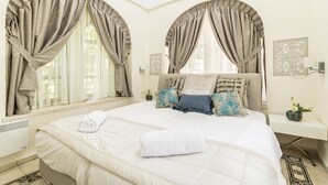A bedroom with a large bed, two bedside tables, a nightstand, and a window with curtains.