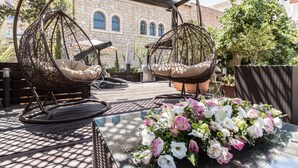 A patio with two wicker swing chairs, a glass table with a floral arrangement, and a stone building in the background.