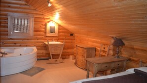 Une chambre à coucher aménagée dans un chalet en rondins, avec un intérieur en bois, une grande baignoire, une commode en bois et une petite table.
