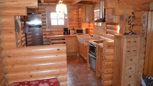 Une cuisine rustique, située dans une cabane en bois, équipée d’un réfrigérateur, d’un four à micro-ondes, d’une cuisinière et de meubles de rangement en bois.