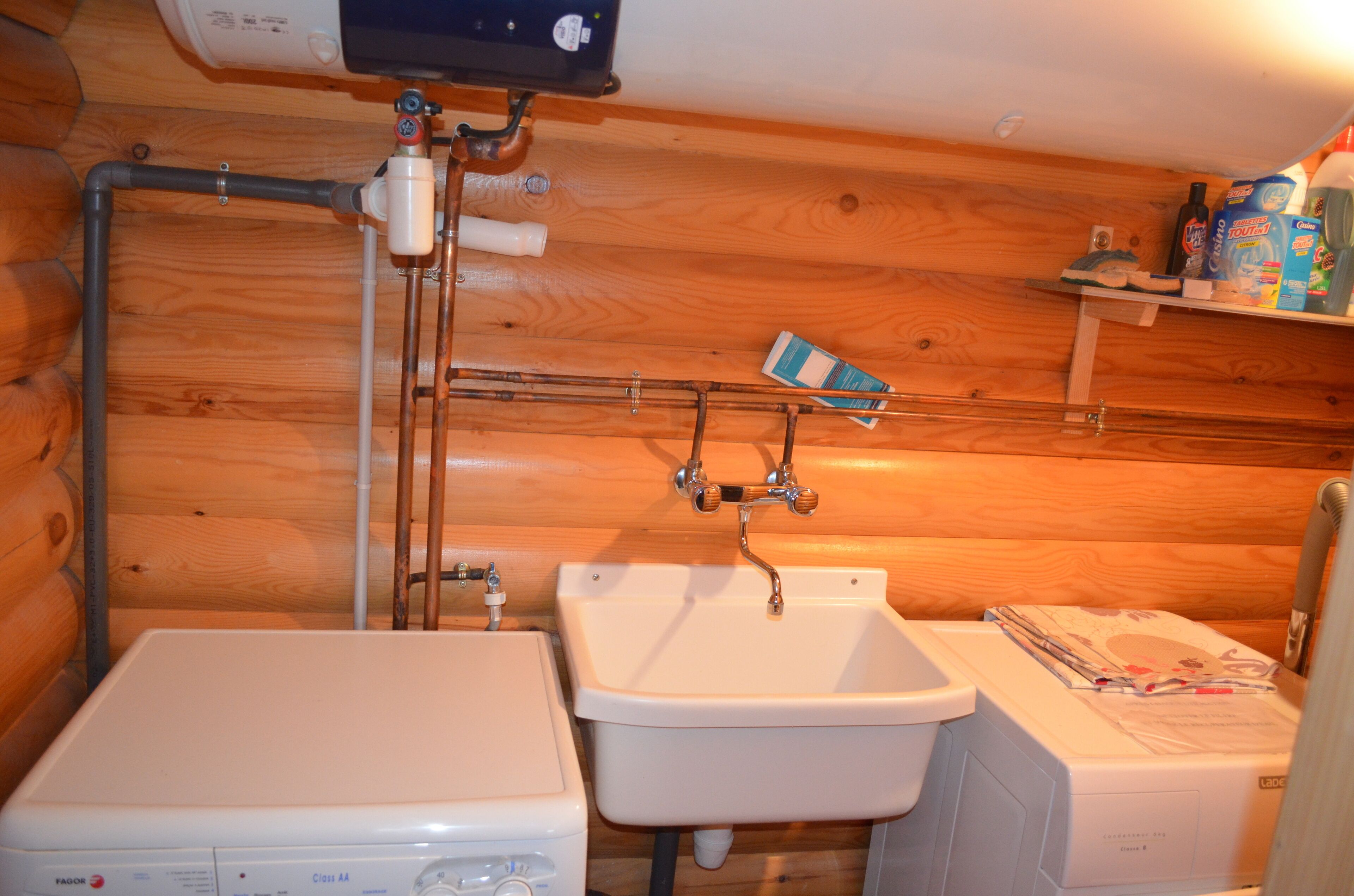 Un baño rústico en una cabaña de madera, con lavadora, lavamanos y retrete.