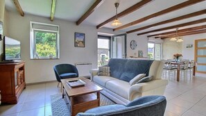 A living room with a sofa, armchair, and wooden coffee table. There is a window, a clock, and a door leading to another room.