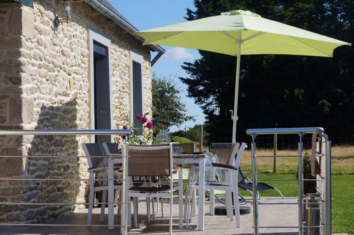 Un espace extérieur aménagé avec des murs en pierre, une table entourée de chaises, un parasol jaune et une rambarde en métal.