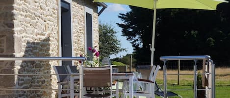 Un espace extérieur aménagé avec des murs en pierre, une table entourée de chaises, un parasol jaune et une rambarde en métal.
