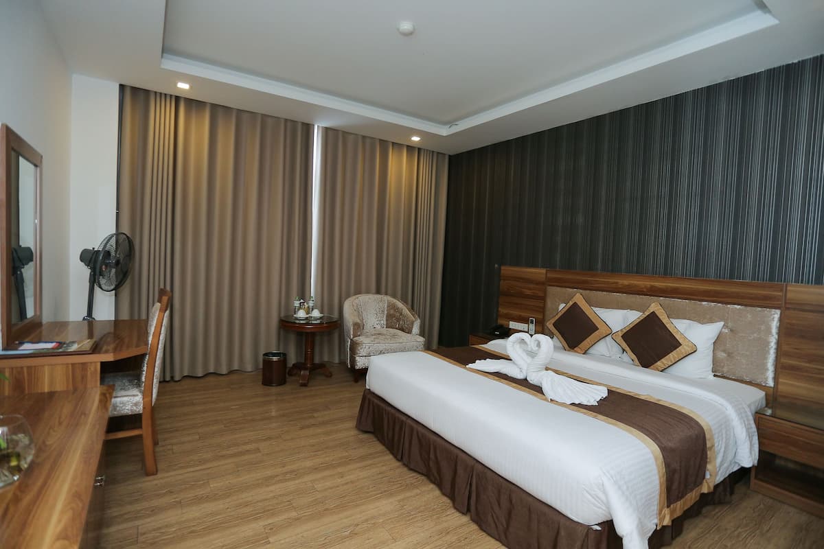 Hotelkamer met een groot bed, een houten bureau, een stoel en een tafeltje met een ventilator.