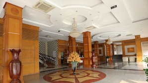 A lobby with a large wooden reception desk, a central floral arrangement, and a chandelier. - Central Phu Hung Hotel (Quang Phu)