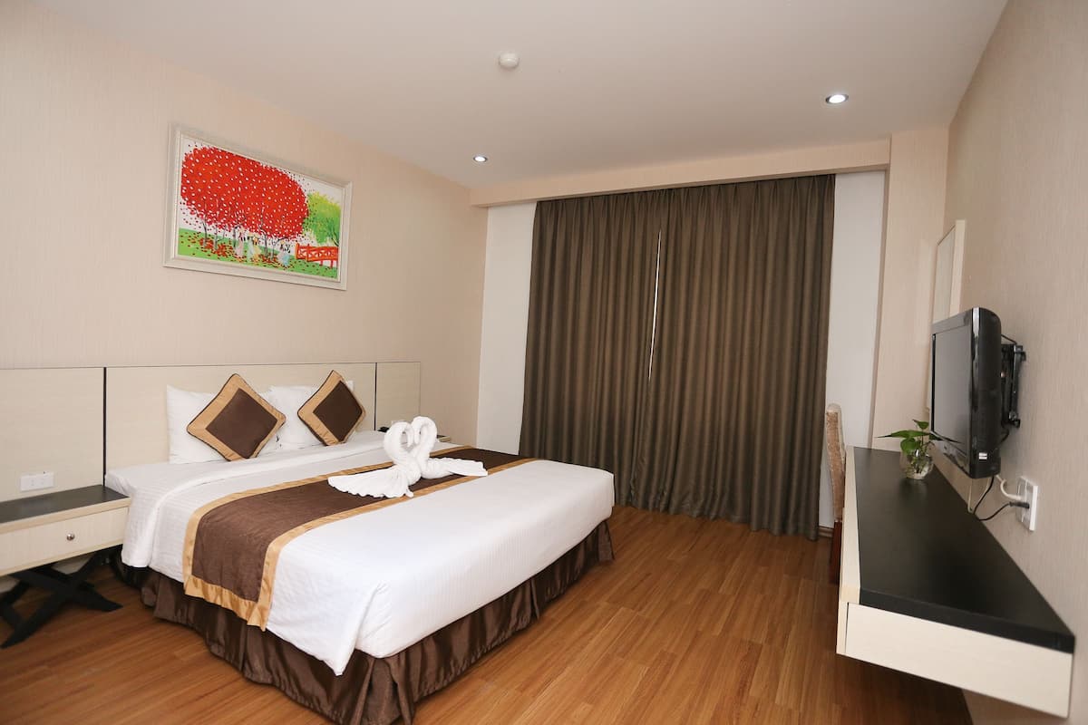 Een hotelkamer met een bed, een bureau, een televisie en een schilderij aan de muur.