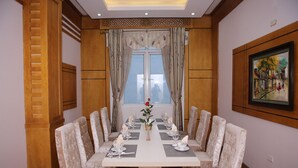 A dining room with a long table set for a meal, flanked by wooden paneling and a large window with curtains. - Central Phu Hung Hotel (Quang Phu)