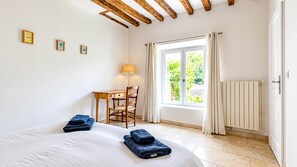 Una camera da letto con un letto, una scrivania, una sedia, una finestra con tende e un termosifone.