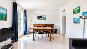 Uma sala moderna com televisão de tela plana, área de jantar com mesa e cadeiras de madeira e um sofá preto.