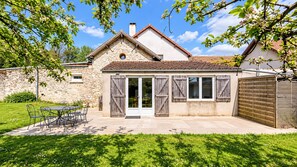 A two-story house with a stone facade, a tiled roof, and a patio with outdoor furniture. - Le Cottage - Ferme de Pontaly (BAILLY)