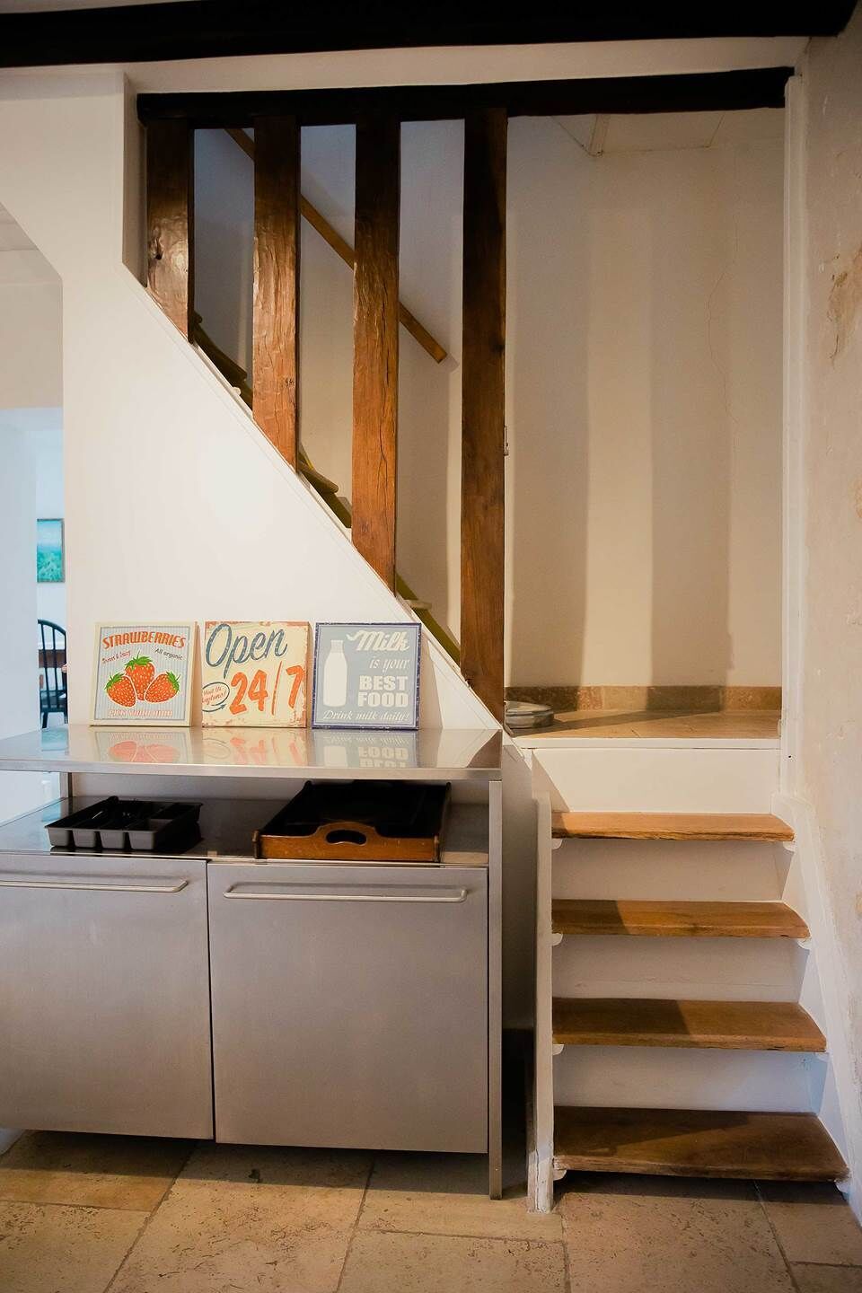 Una escalera con escalones de madera y una pared blanca. Se observan letreros en la pared anunciando 'fresas' y 'abierto las 24 horas'.