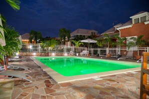 A swimming pool with lounge chairs and umbrellas, surrounded by a stone patio and palm trees. - Etal Paradise, a Tropical Paradise in Sainte-Anne in Guadeloupe (SAINTE ANNE)