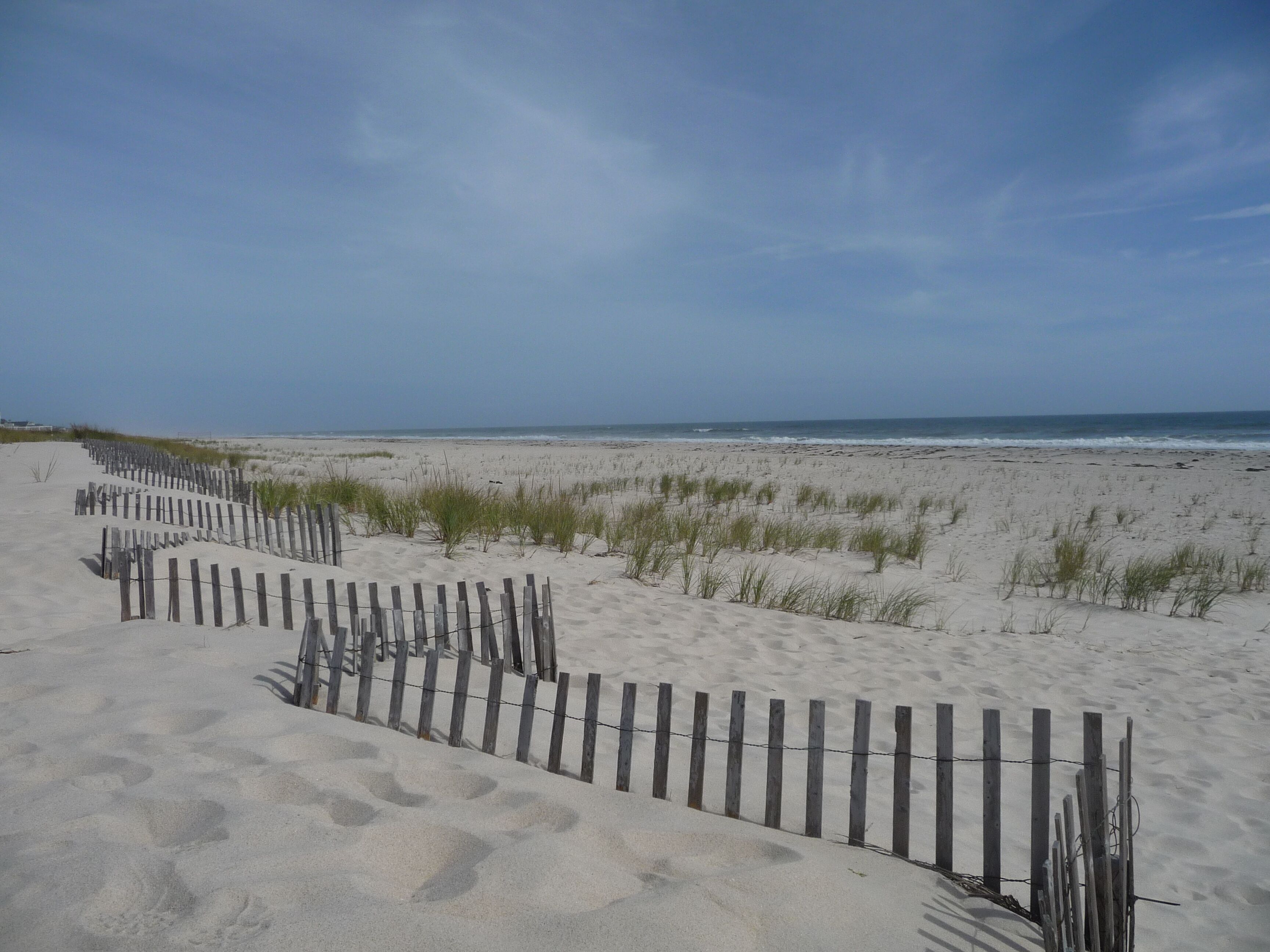 A sandy beach with a wooden fence and grass in the foreground.