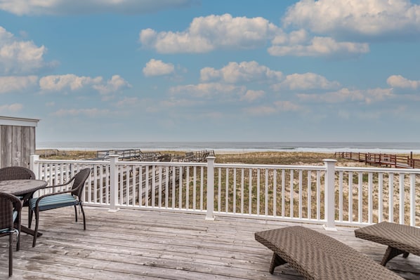 Una terraza de madera con mobiliario de mimbre con vista a una playa.