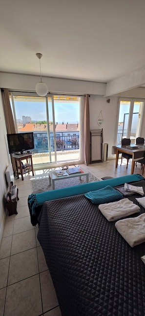 A hotel room with a bed, a TV, a balcony with a view, a table, and a chair.