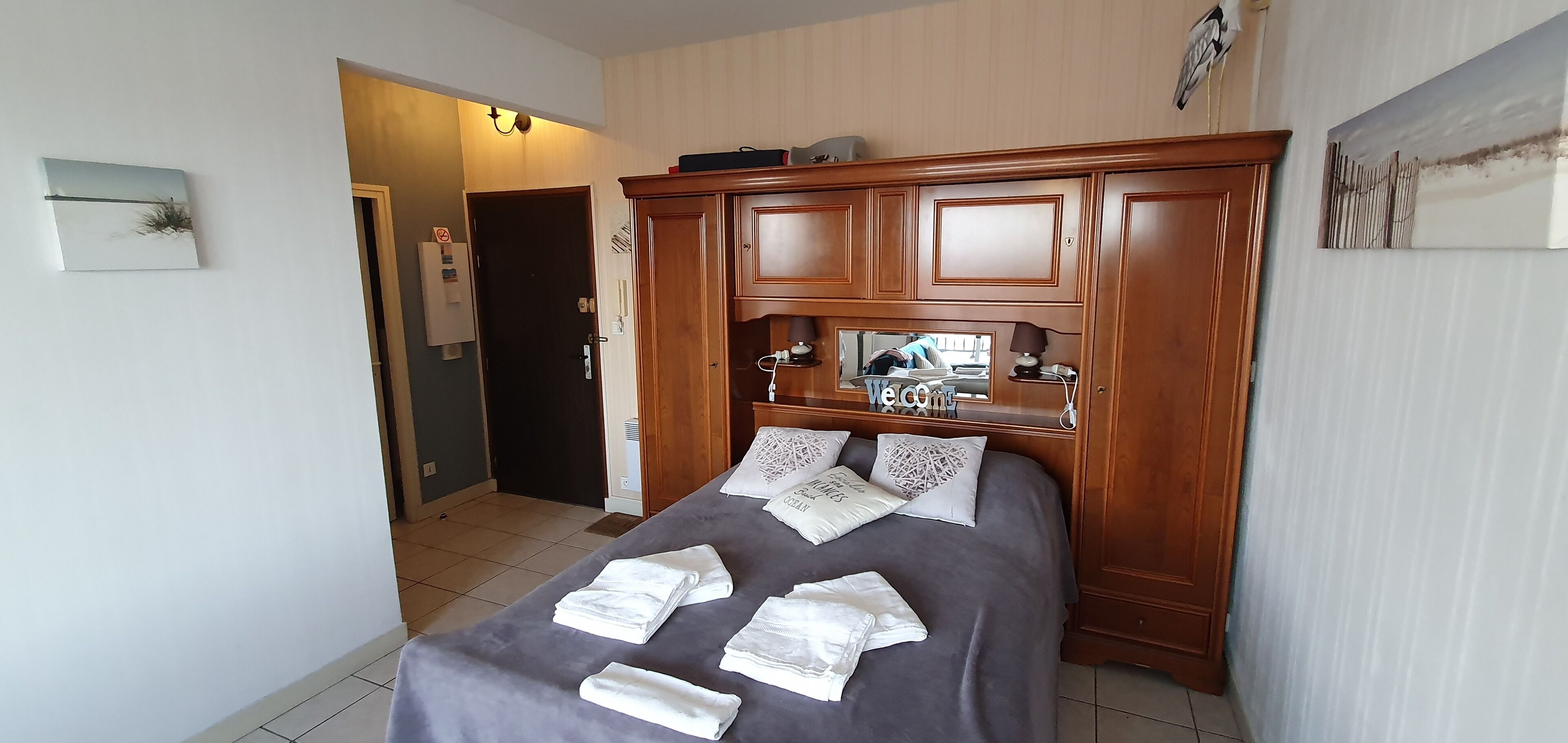 Ein ordentlich bezogenes Bett mit Handtüchern, einem Holz-Kopfteil und einem Willkommensschild.