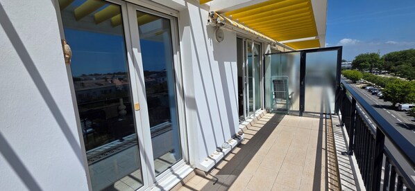 A balcony with glass doors, a yellow awning, and a view of a street with parked cars and trees. - Appt 4 °,top floor, sea view, very bright facing south. WIRELESS. 82cm tvscreen. (Royan)