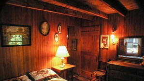 Una habitación acogedora con paredes de madera, una cama con colcha floral, un escritorio con lámpara y una ventana con vistas.