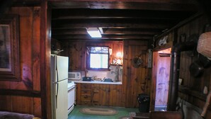 Cocina compacta con paredes de madera, refrigerador, microondas, lavamanos y una ventana sobre el lavamanos.