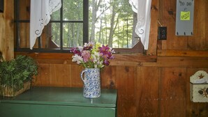 Interior de una cabaña de madera con una ventana, un florero y una señal en la pared.