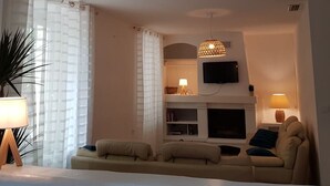 Una sala de estar con sofá, televisor montado en la pared, chimenea y lámpara colgante.