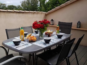 Une table à manger installée à l’extérieur, avec des chaises, un vase de fleurs rouges et divers aliments.