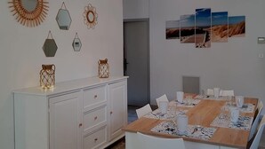Comedor con mesa de madera dispuesta para seis personas, sillas blancas y un mueble blanco con cajones.