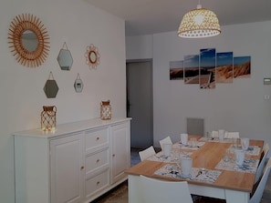 Un coin repas avec une table en bois dressée pour six personnes, des chaises blanches et un buffet blanc avec des tiroirs.