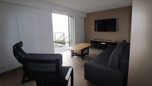Een moderne woonkamer met een bank, een fauteuil, een salontafel en een aan de muur bevestigde televisie.