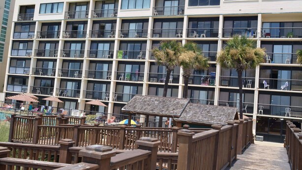 A multi-story hotel with balconies, outdoor seating, and palm trees.