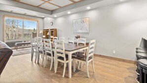 A dining area with a wooden table and white chairs, a bench, and a bookshelf.